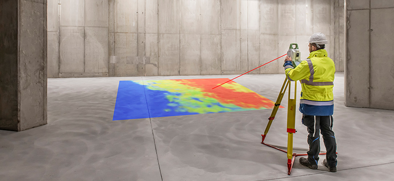A construction surveyor scans a concrete floor with a total station