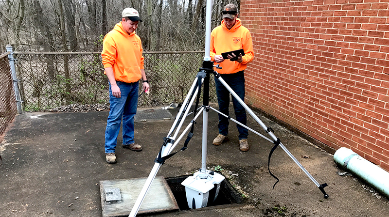 Two young surveyors observe a Leica ScanStation 3D laser scanner mounted upside down in a manhole.