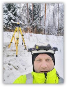 A surveyor measuring with a total station in a snowy forest clearing 